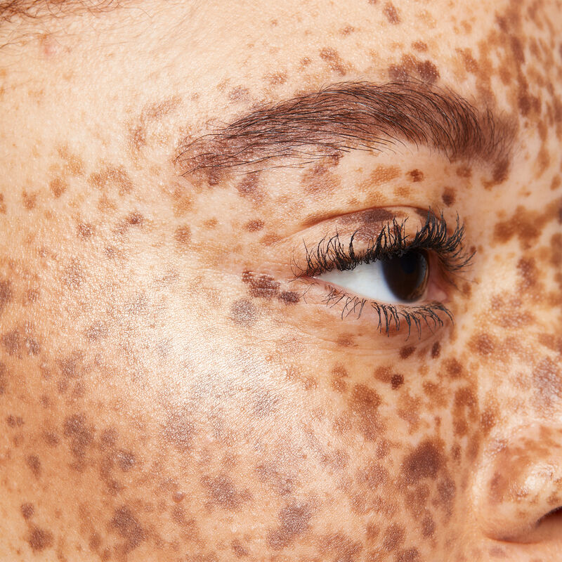 Close-up of medium-skinned model with reddish brown hair, brown eyes and many freckles wearing limited-edition Mary Kay Illuminating Highlighter