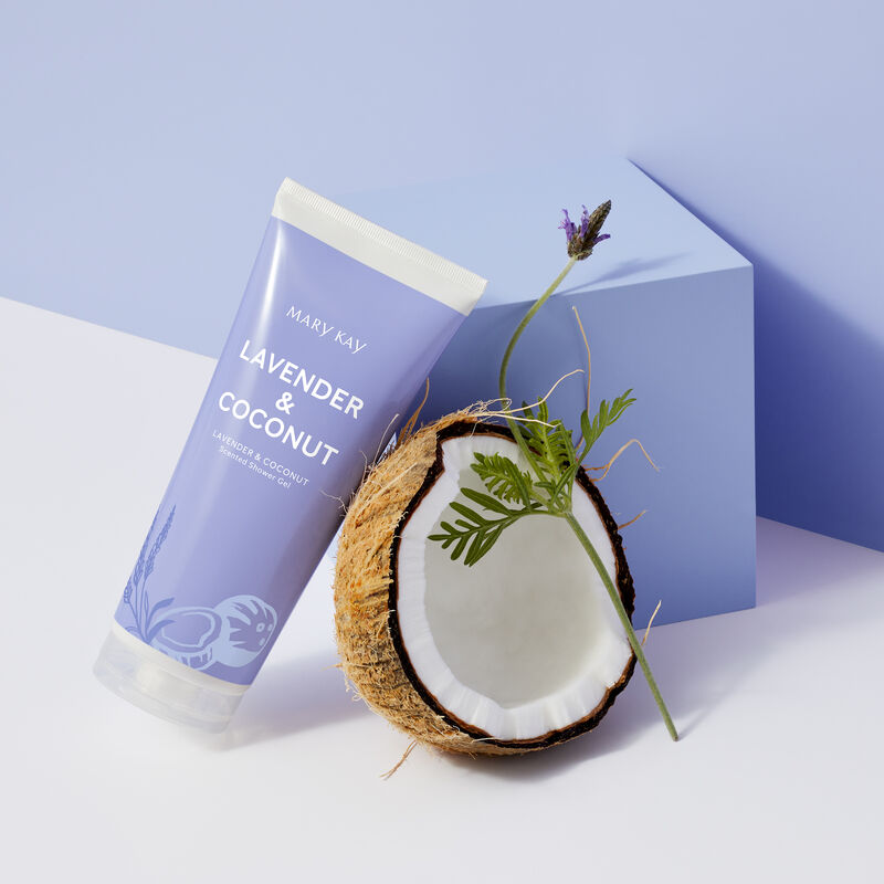 Bottle of limited-edition Lavender & Coconut Mary Kay Shower Gel next to an open coconut and a lavender stem, leaning against a light purple cube